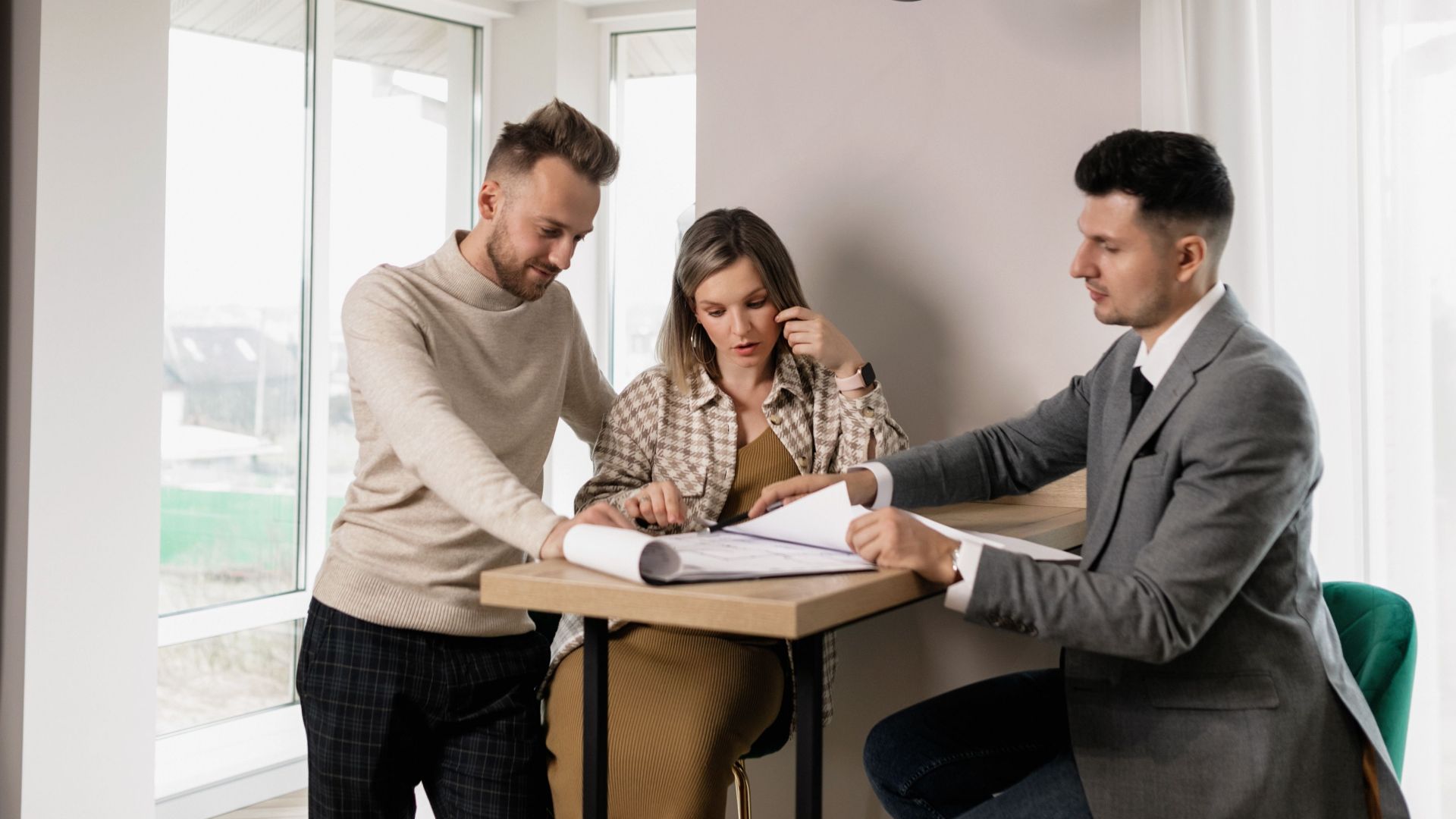 A couple consults with a real estate agent in a modern indoor setting, reviewing property documents.
