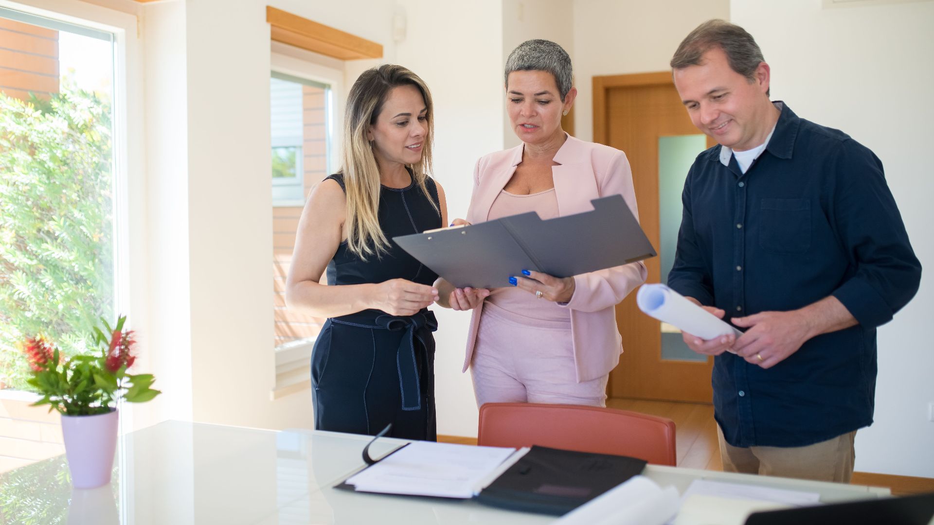 Three real estate professionals examining documents in a modern office setting, focusing on a property sale.
