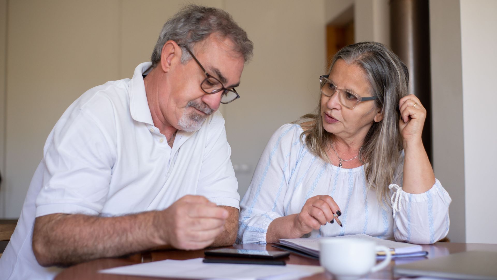 Senior couple reviewing documents and managing finances together at home, showing collaboration and care.