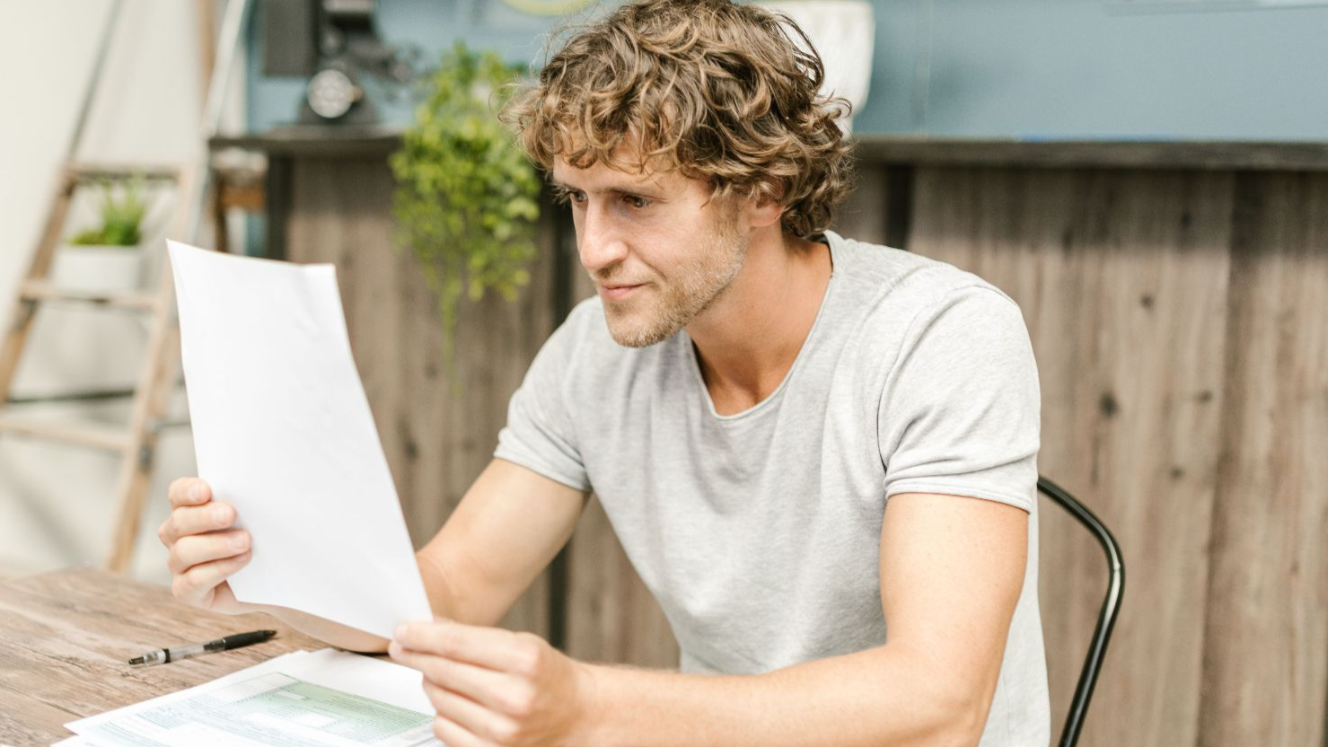 A man with curly hair evaluates documents at a desk, highlighting focused work in a professional setting.
