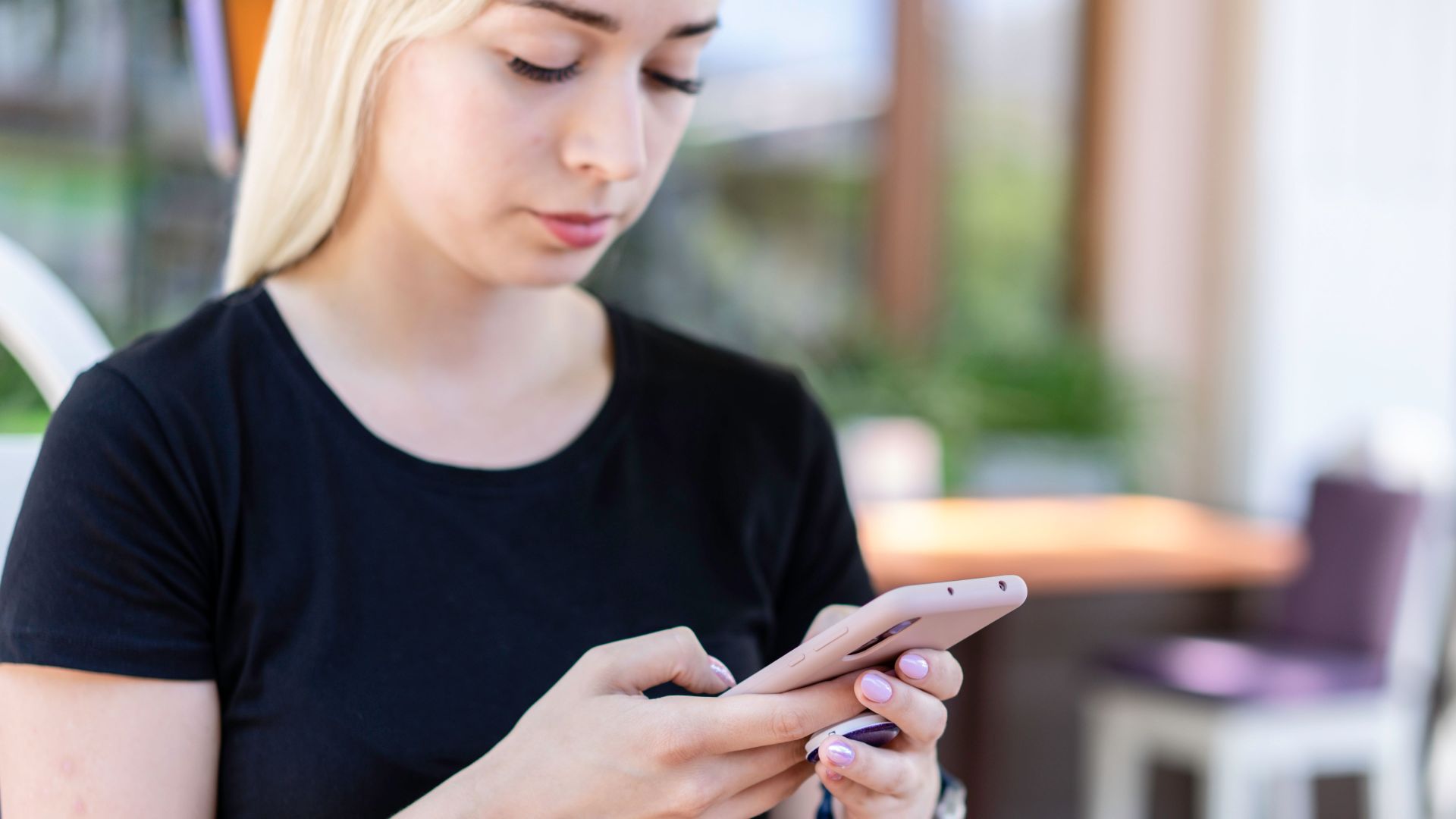 Young woman in a black shirt texting on her smartphone at an outdoor cafe.