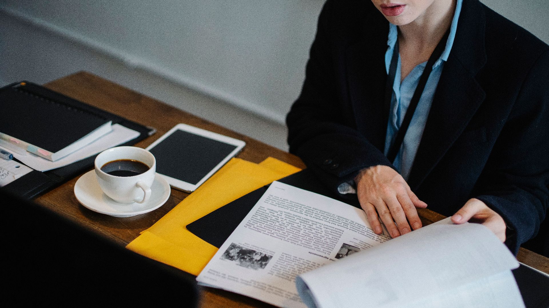 High angle of crop faceless businesswoman in formal clothes sitting at table with tablet and hot coffee and looking through documents