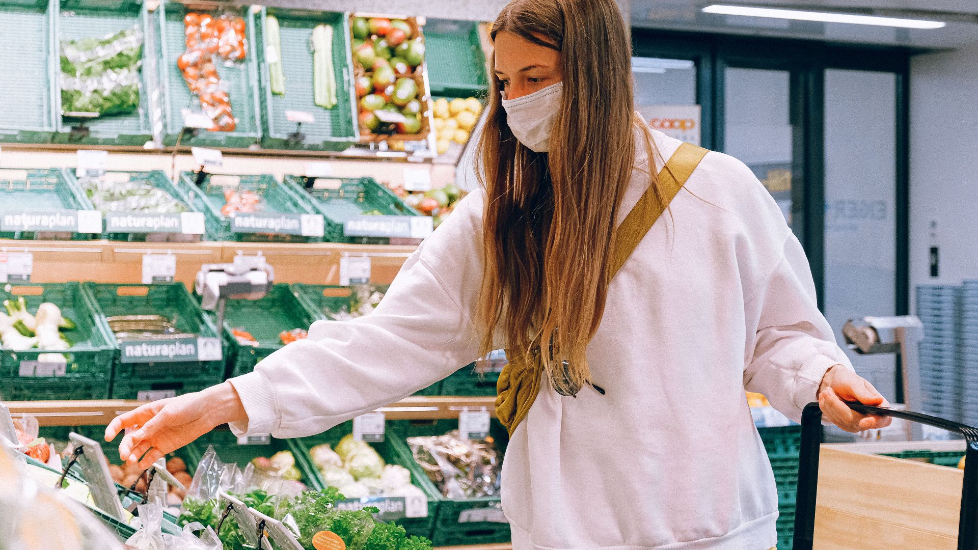 Woman wearing a face mask shopping for vegetables in a grocery store during the pandemic.