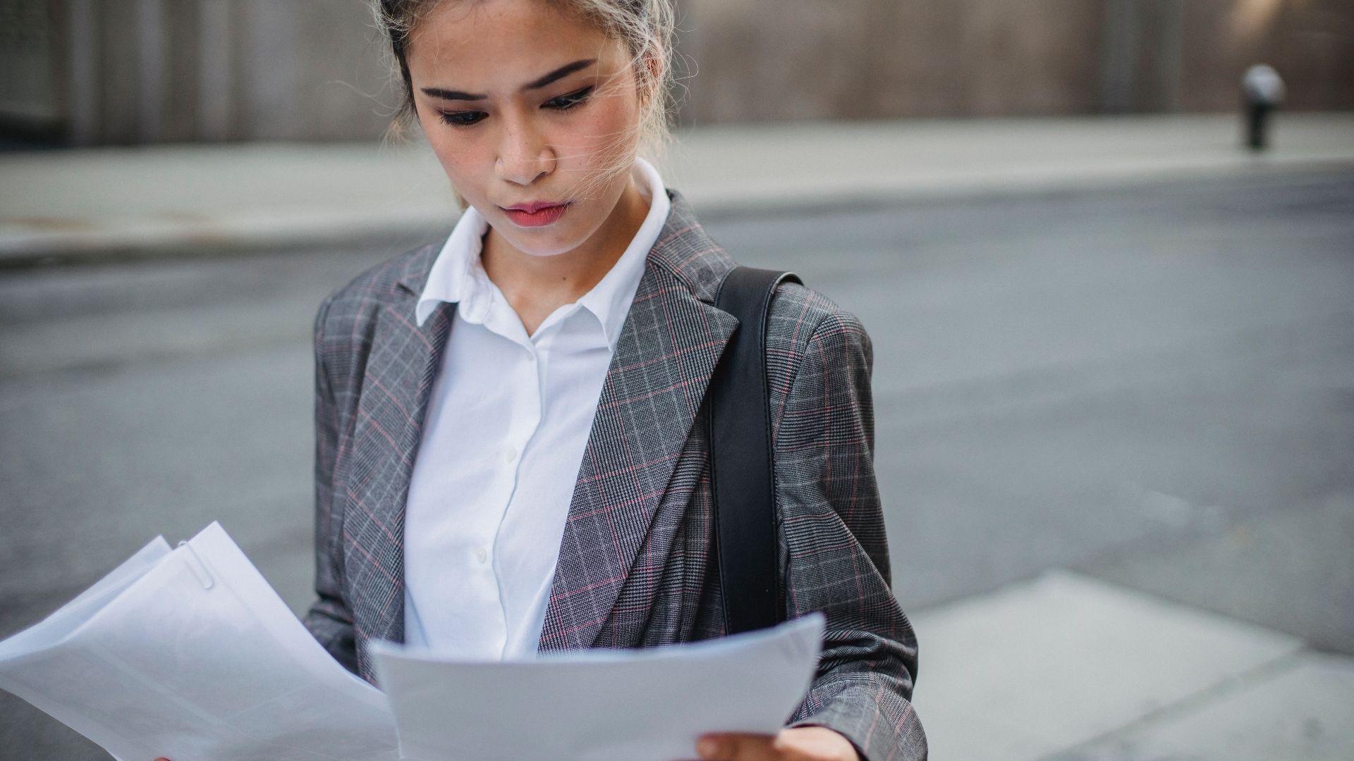 Focused businesswoman in a suit reviews important papers outdoors.