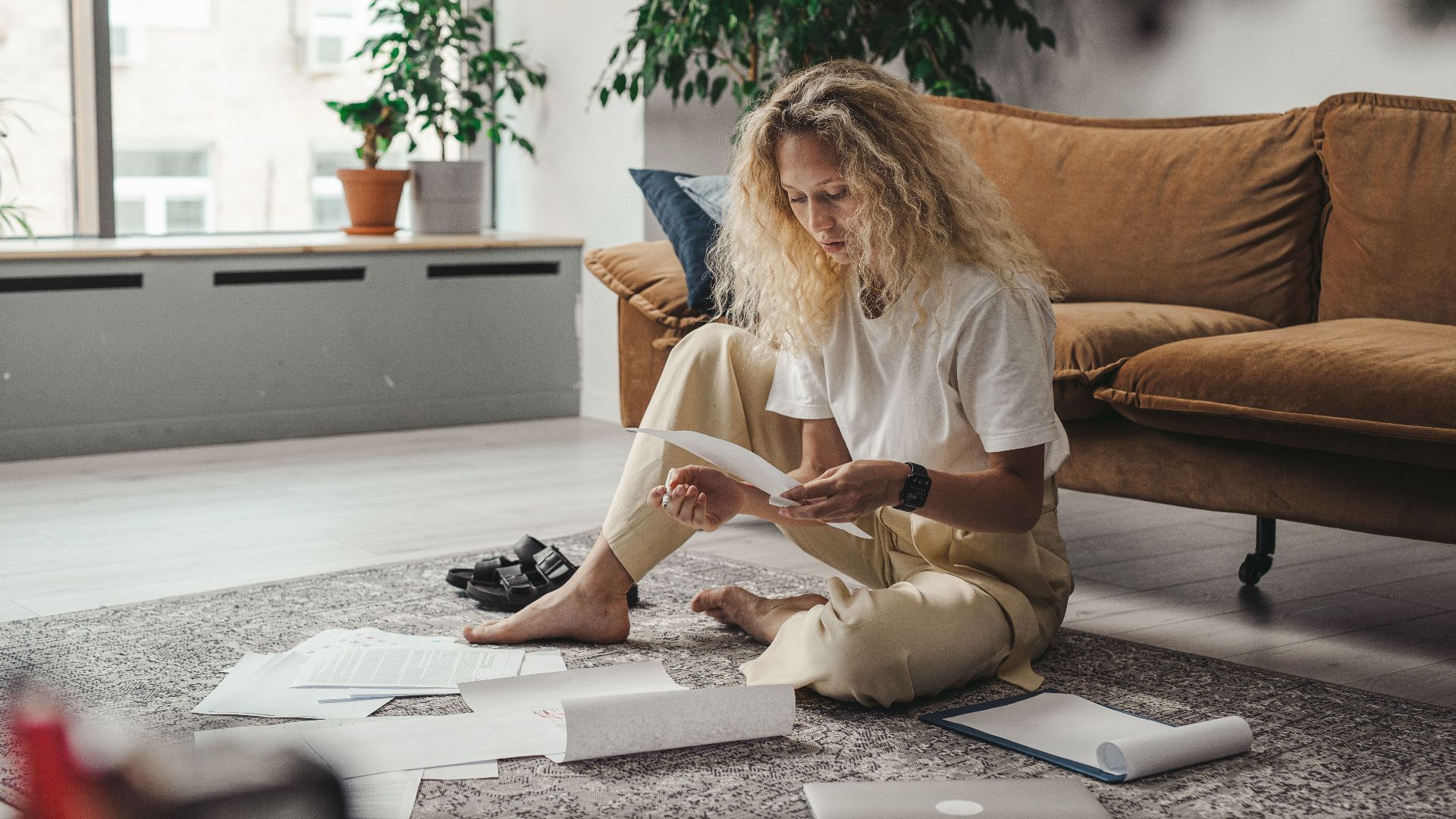 Woman sitting on the floor at home, reviewing paperwork in a relaxed environment.