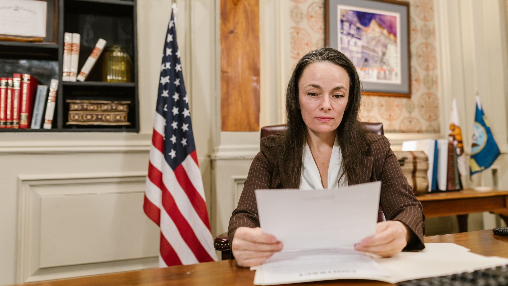 A professional woman reviewing legal documents in an office with flags and books.