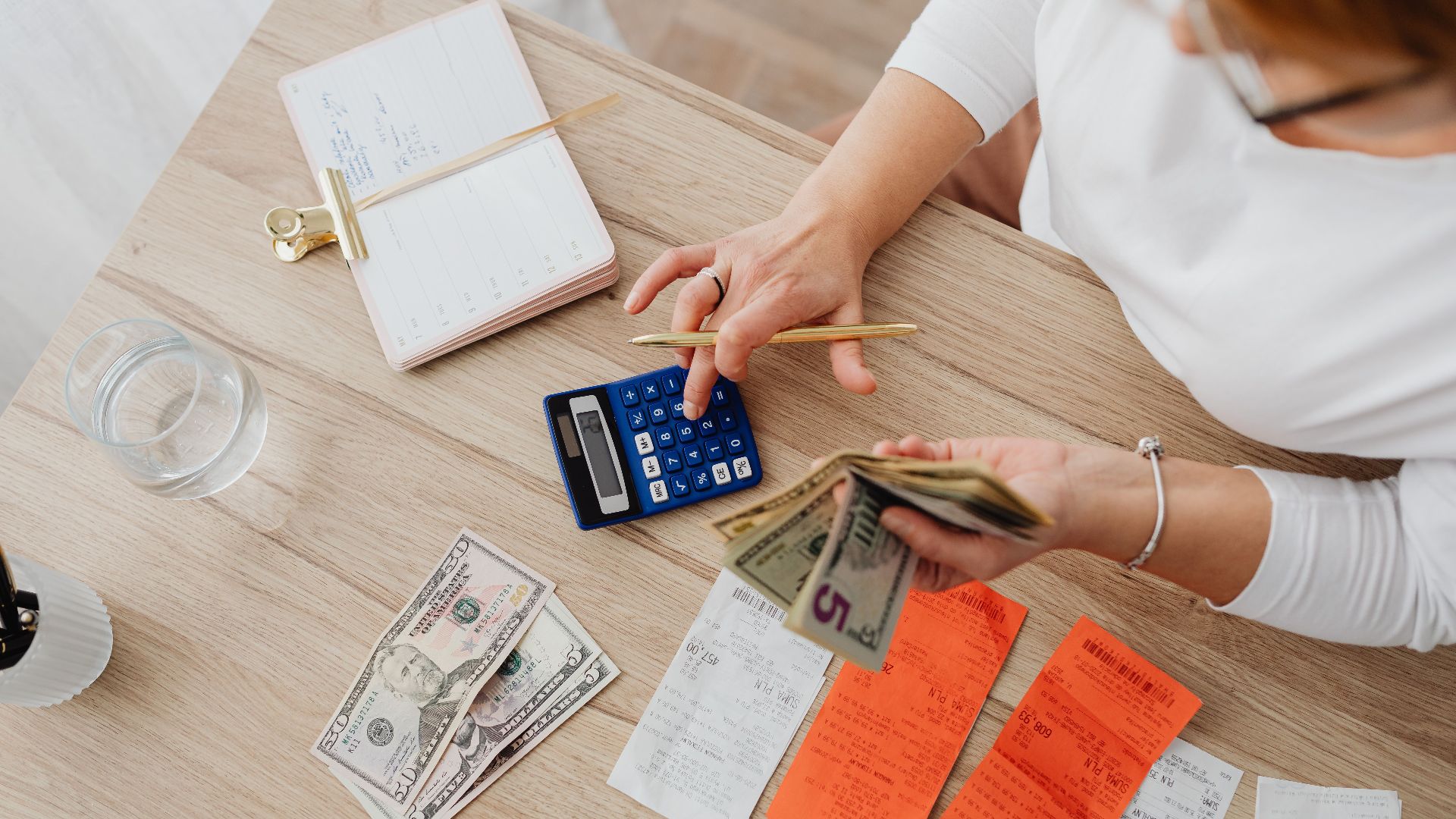 Overhead view of a person using a calculator to manage cash and receipts at a desk.
