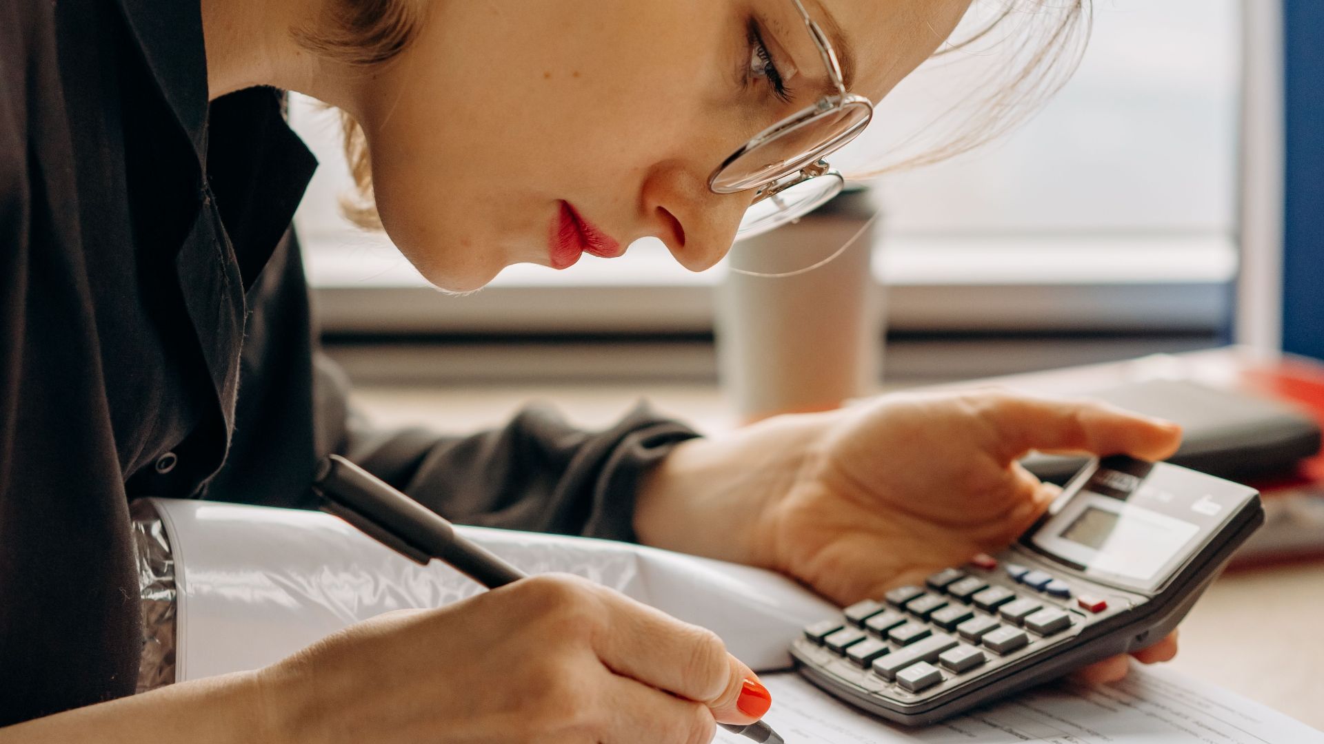 Woman with eyeglasses concentrating on financial calculations with notebook and calculator.