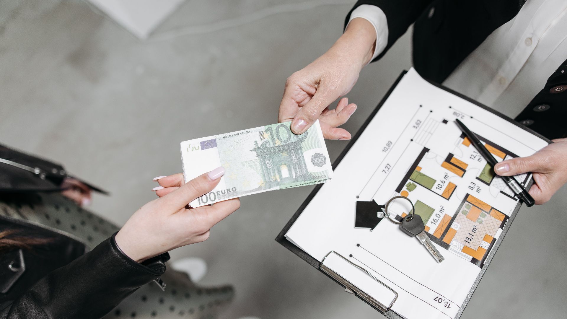 Close-up of a real estate transaction with euro bill, keys, and floor plan.