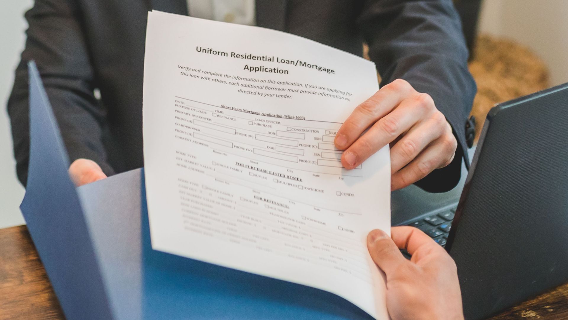 Professional setting showing hands exchanging a mortgage application document indoors.