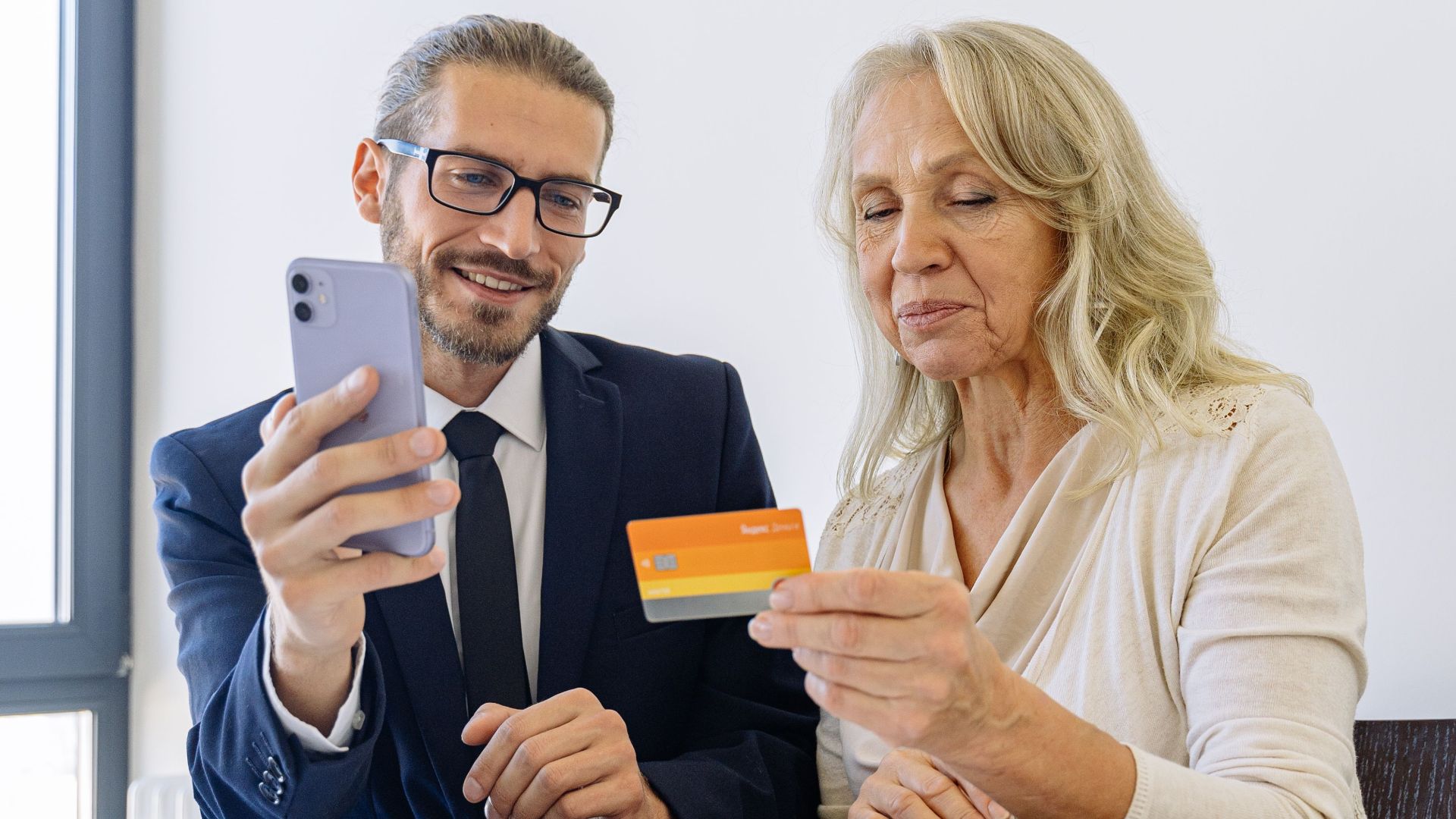Senior woman and businessman discussing finance using smartphone and credit card in office.