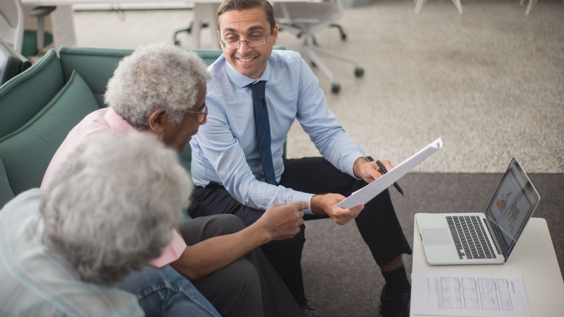 Consultant discussing financial plans with senior clients in a modern office setting, using documents and a laptop.