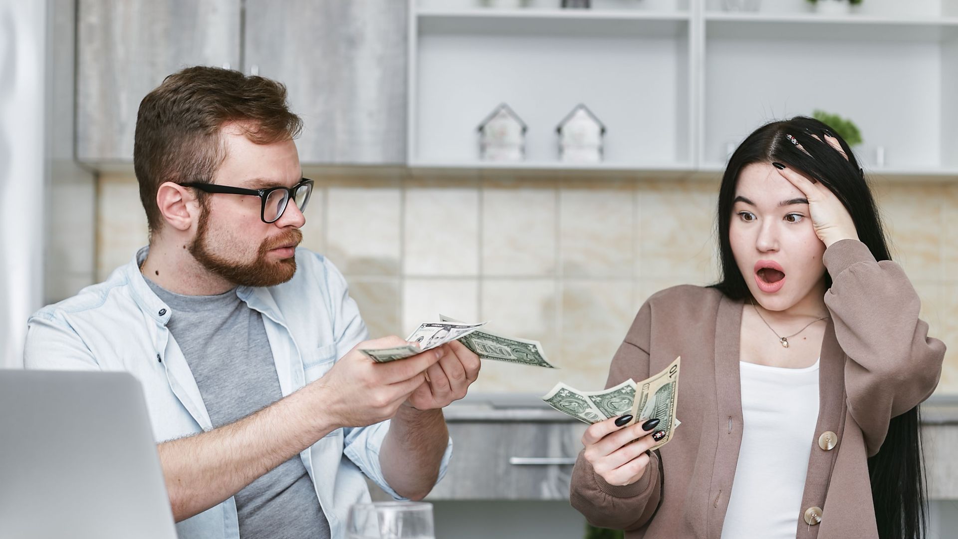 A shocked couple sitting at a table counting cash, illustrating financial surprise.