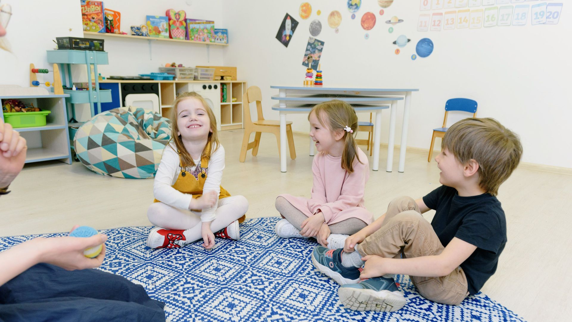 A group of young children happily playing together in a well-decorated kindergarten classroom.