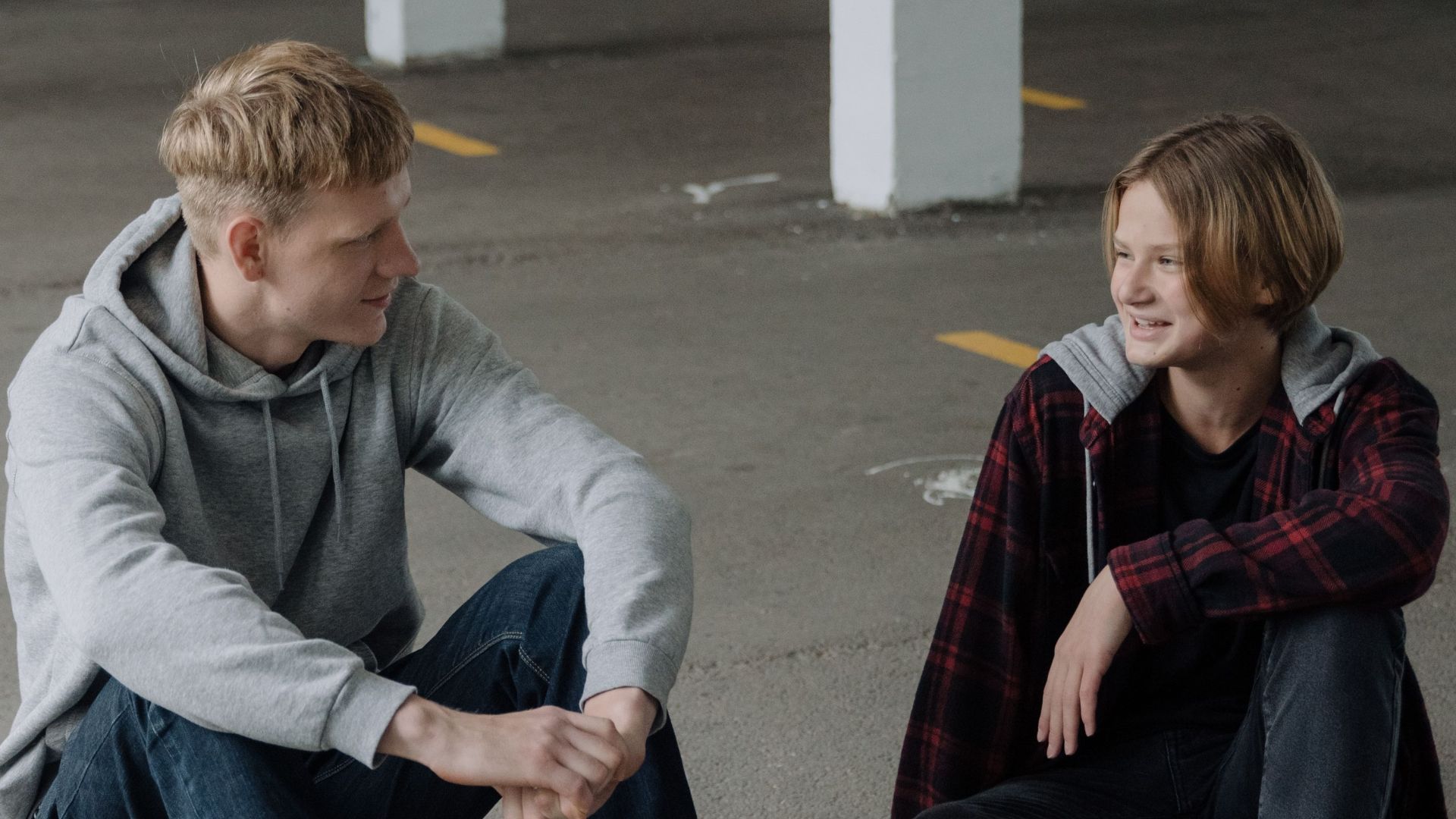 Two teenage skaters sitting and talking in a parking garage.