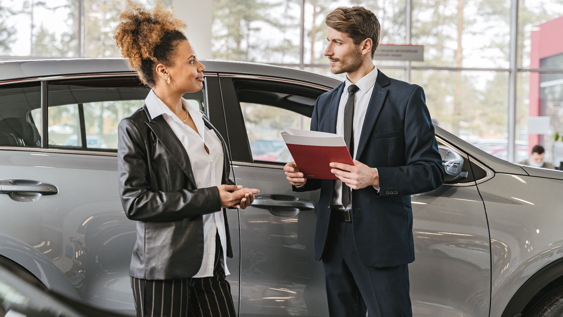 A woman discussing car purchase with a dealer inside a car dealership showroom.