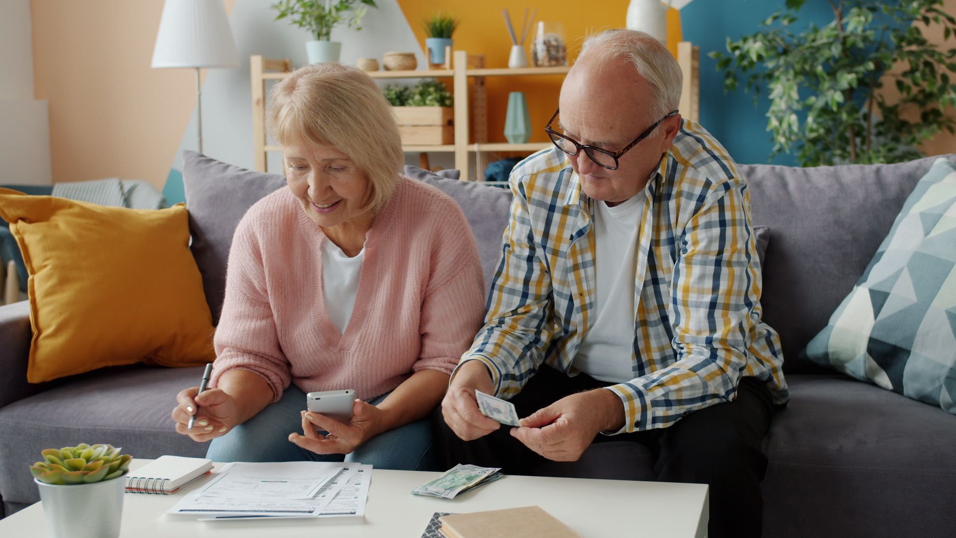 Elderly couple budgeting at home, reviewing bills and managing finances together.