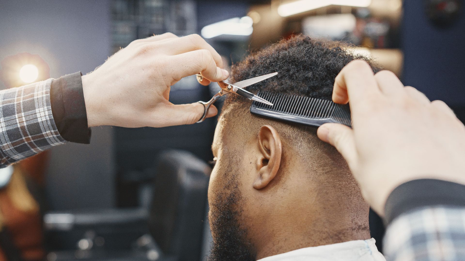 Close-up of a barber giving a haircut with scissors and comb in a modern salon.