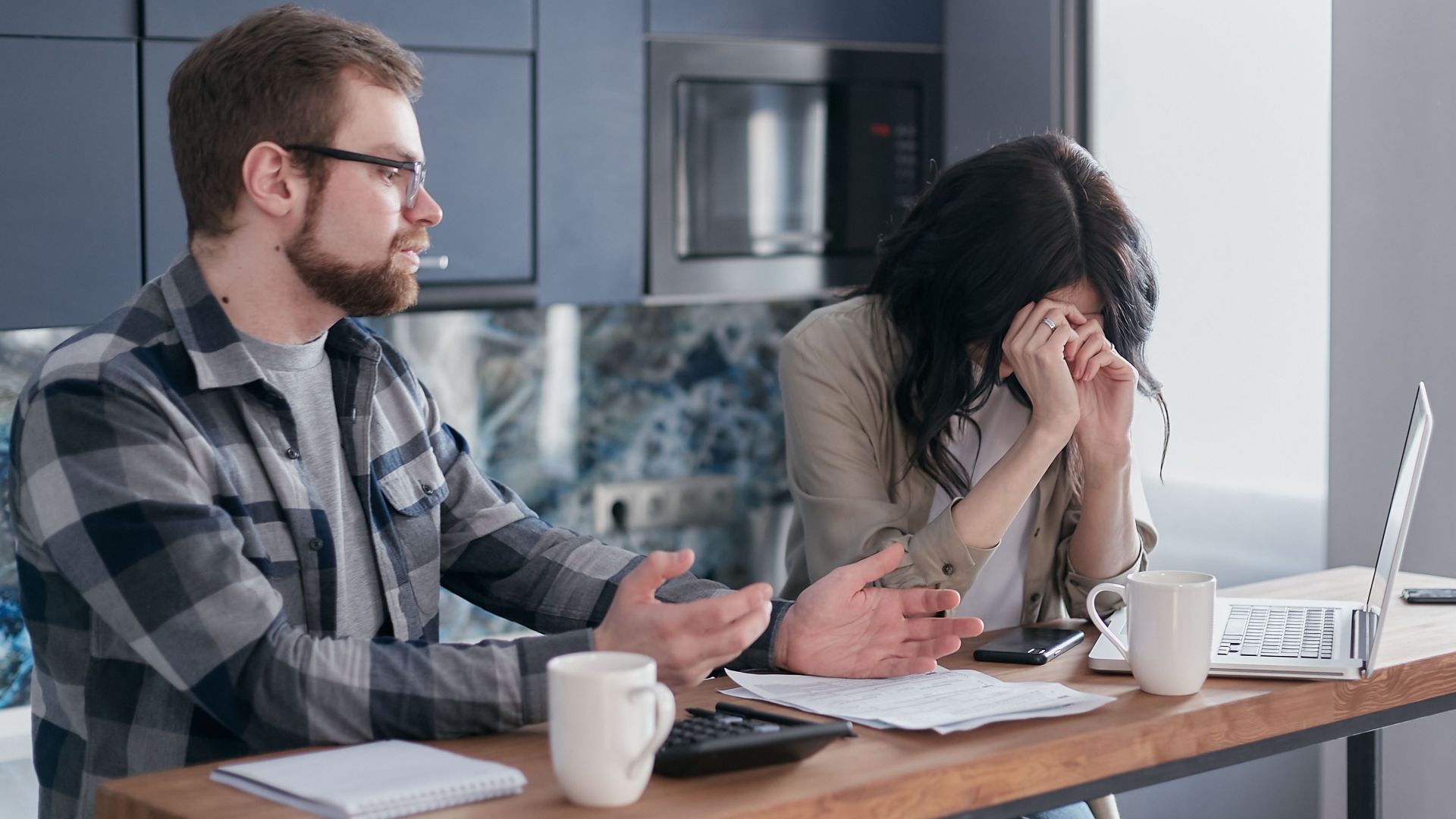 A couple seated at a table, looking stressed while discussing financial issues indoors.