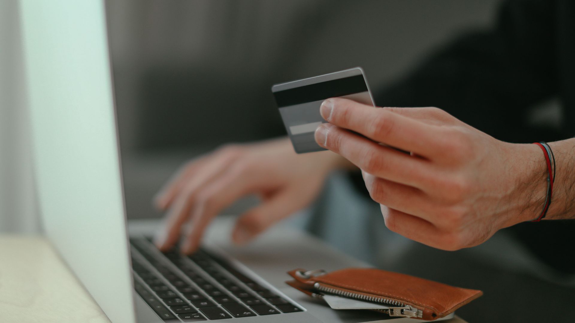 Close-up of a person holding a credit card while shopping online on a laptop.