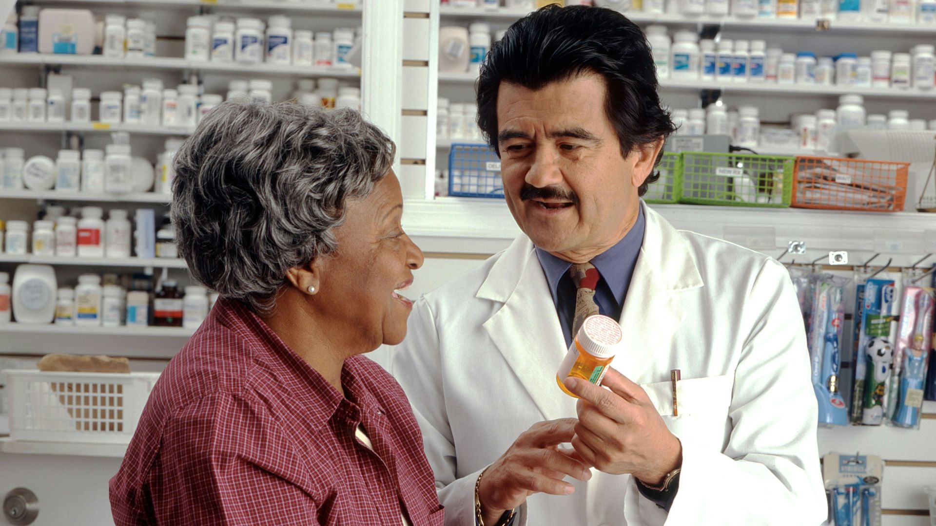 A pharmacist in a white coat showing a pill bottle to a woman