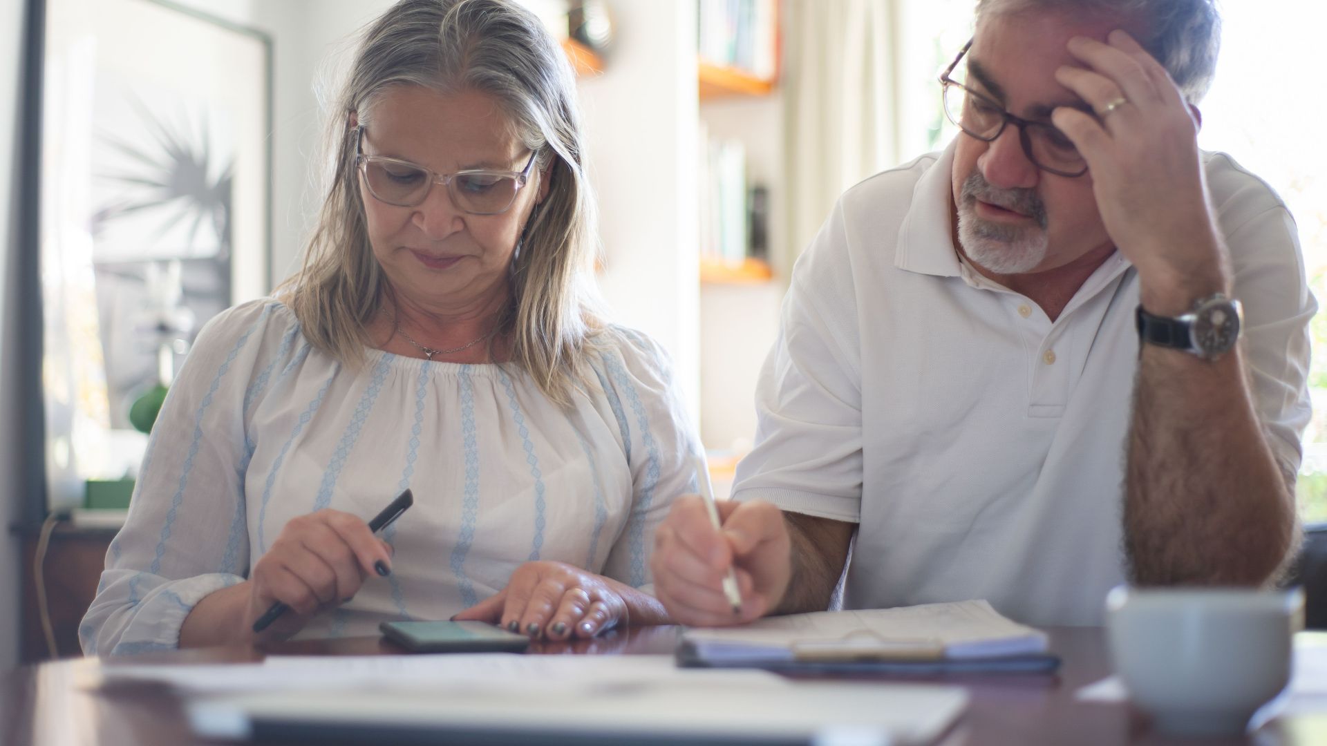 Senior couple calculating expenses at home office desk with documents and notes.