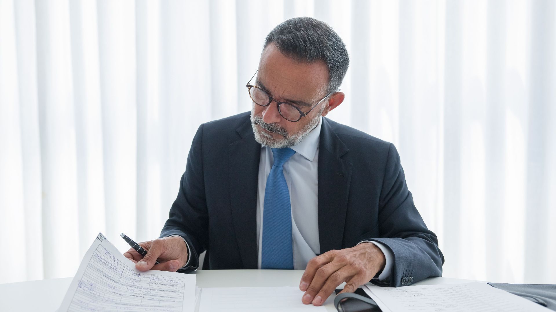 Elderly businessman in suit reviewing documents at desk. Professional setting.