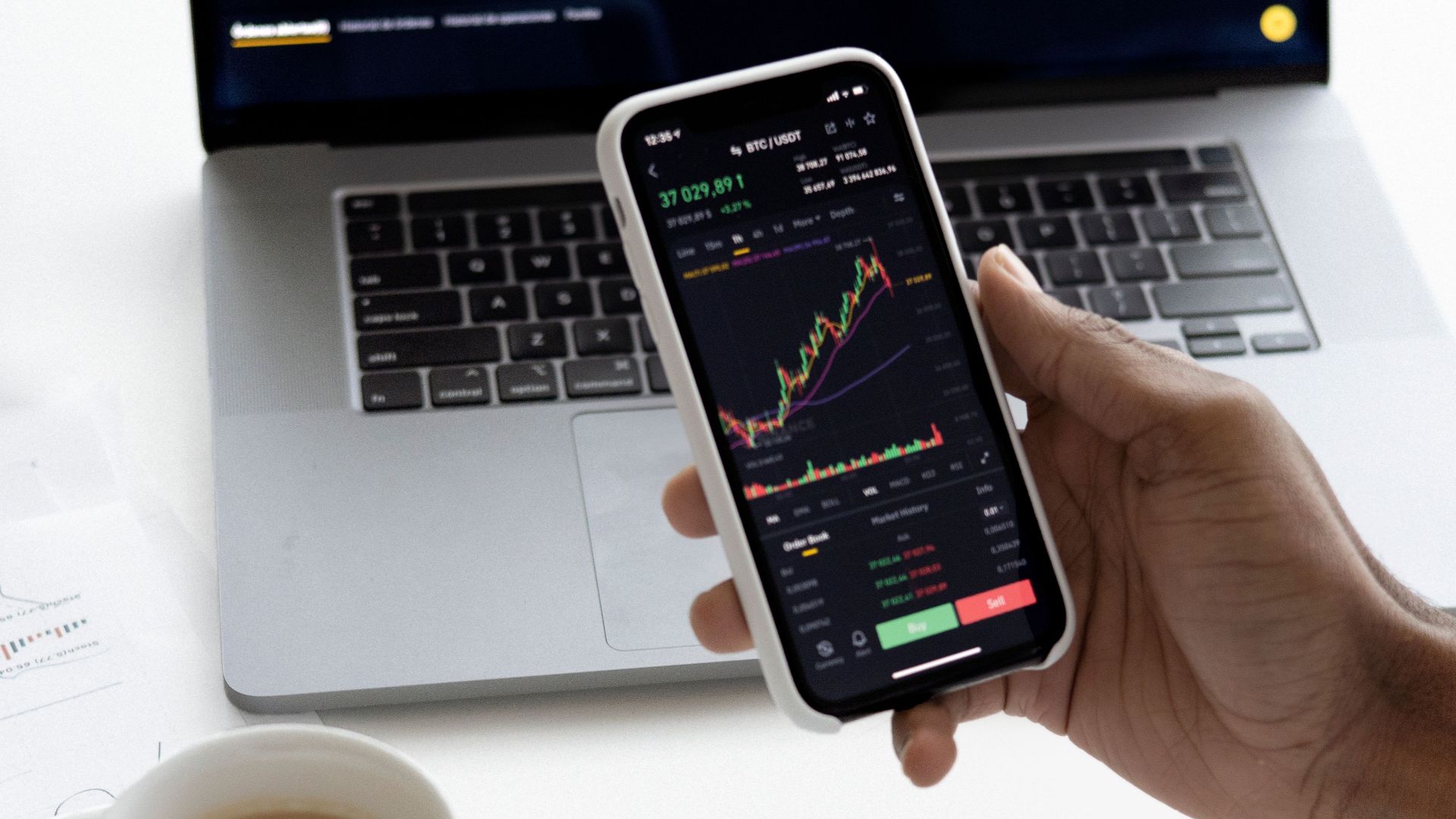 Person analyzing stock market trends on smartphone with laptop background