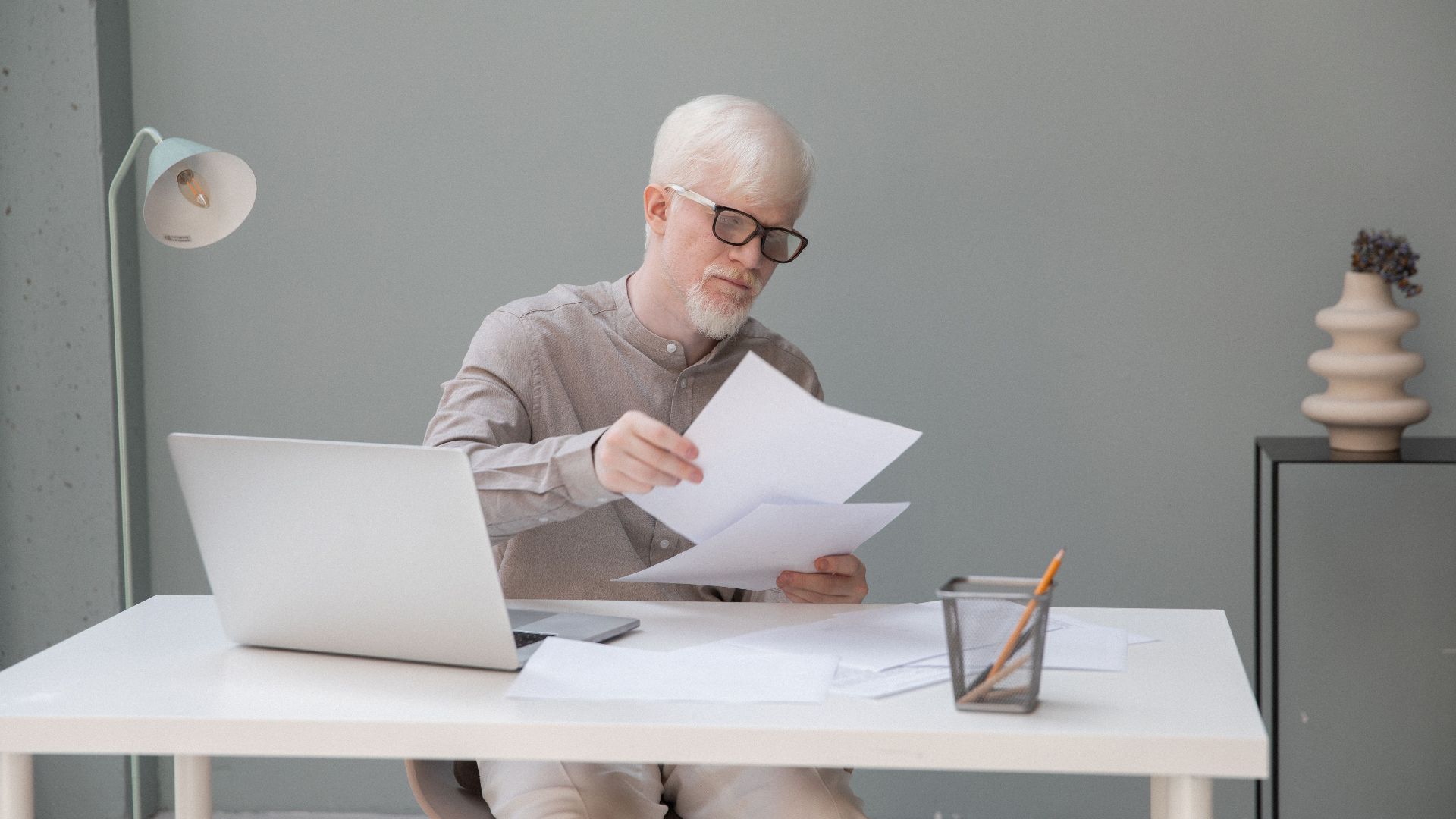 Albino concentrated office worker in eyeglasses watching documents at desk with netbook in daylight