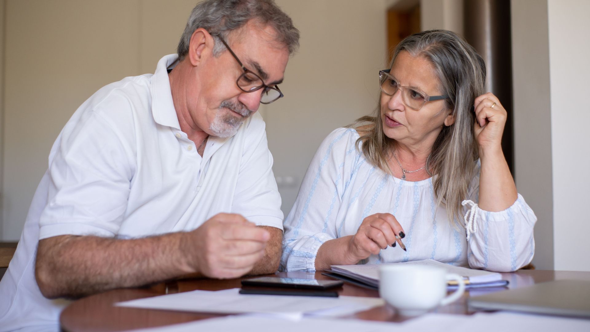 Senior couple reviewing documents and managing finances together at home, showing collaboration and care.