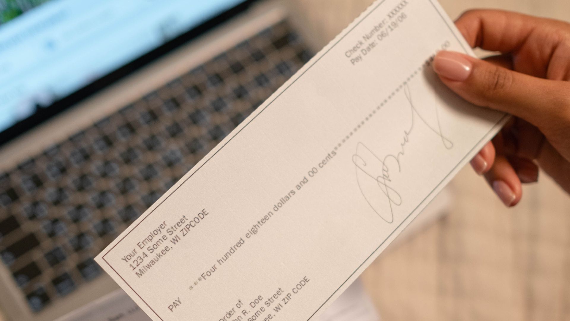 Individual holding a cheque over laptop, signifying online banking or financial transaction.