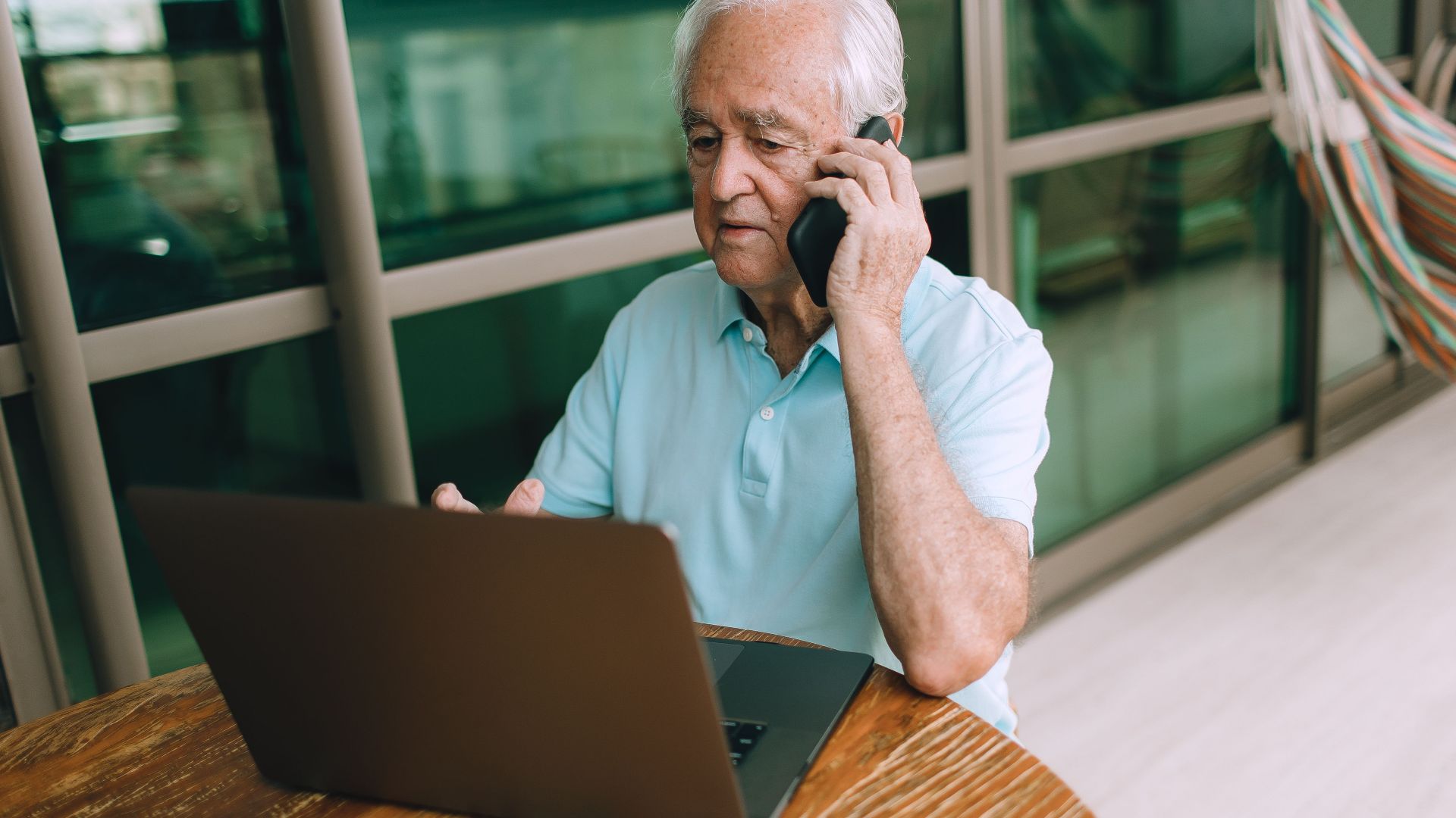 Elderly man multitasking with smartphone and laptop at home.