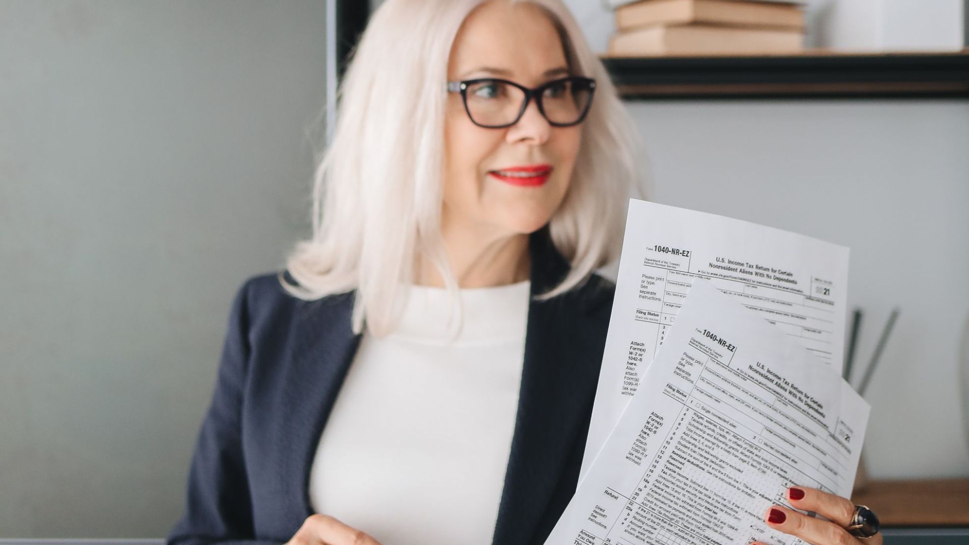 Confident senior woman in glasses holding documents in a modern office setting.