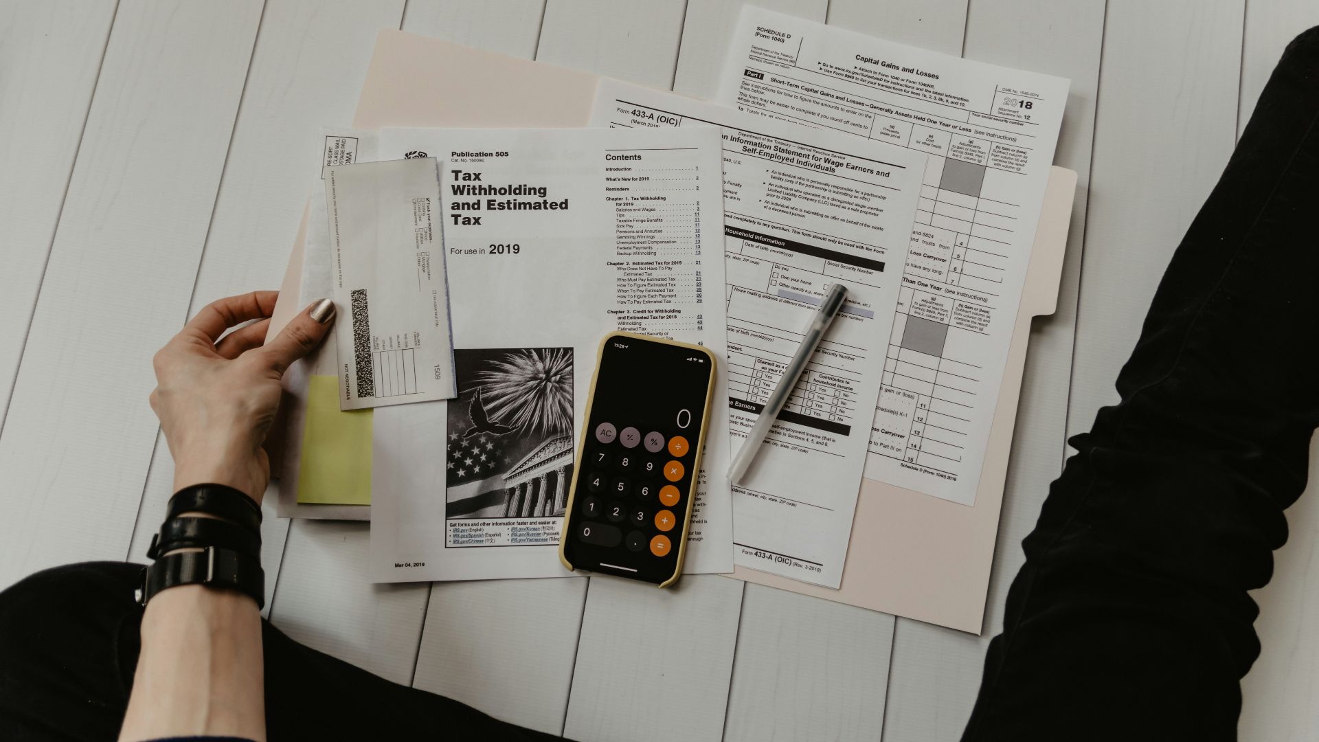 person holding paper near pen and calculator