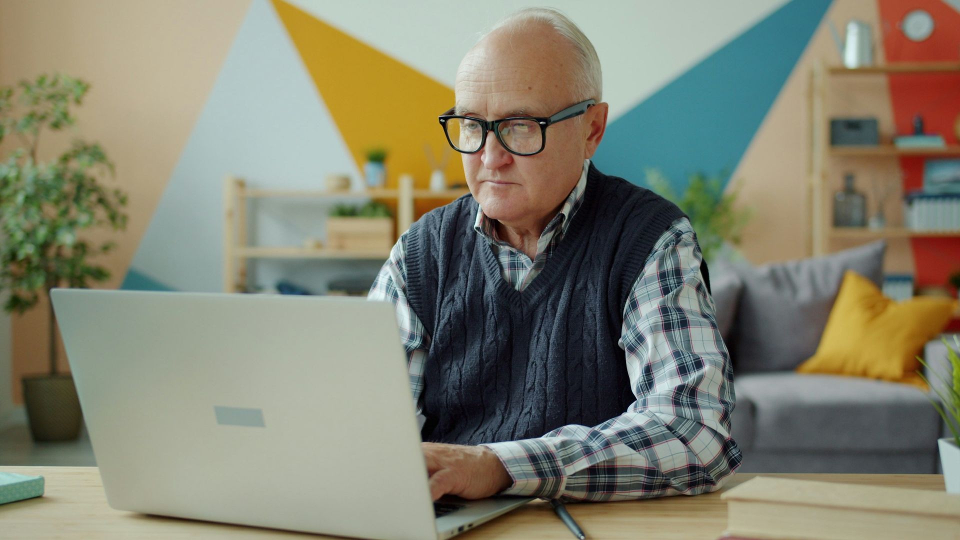 Elderly man wearing glasses using a laptop at home
