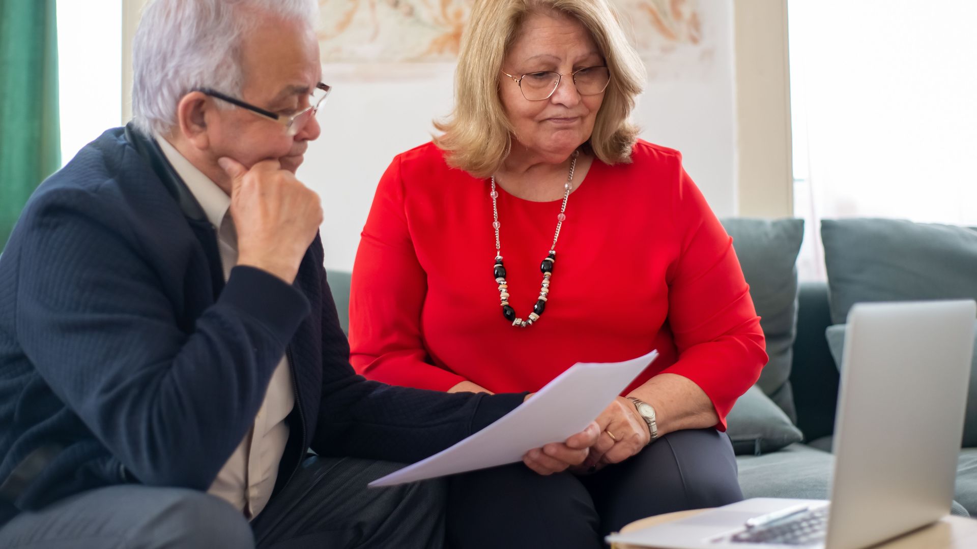 Elderly couple reviewing financial documents together at home in Portugal.