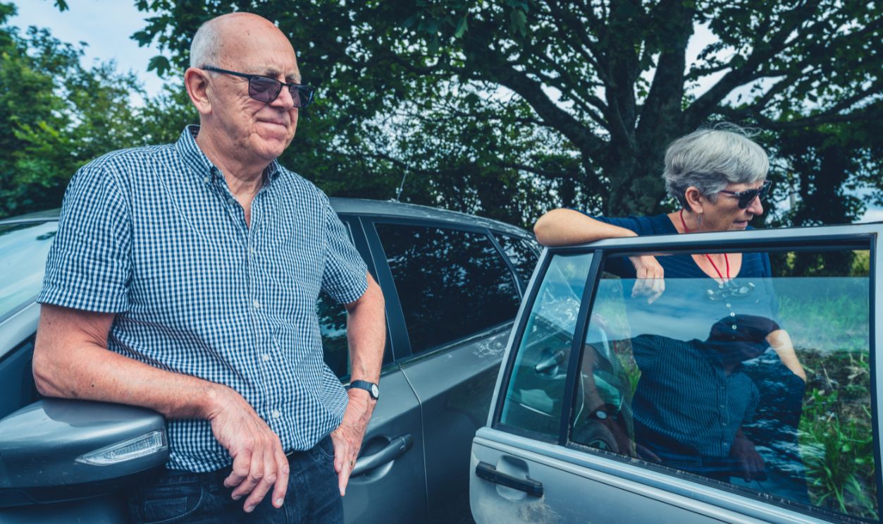 A senior couple are standing by their car