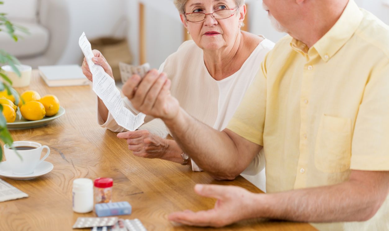 Senior woman reading leaflet of a drug and elderly man holding pills