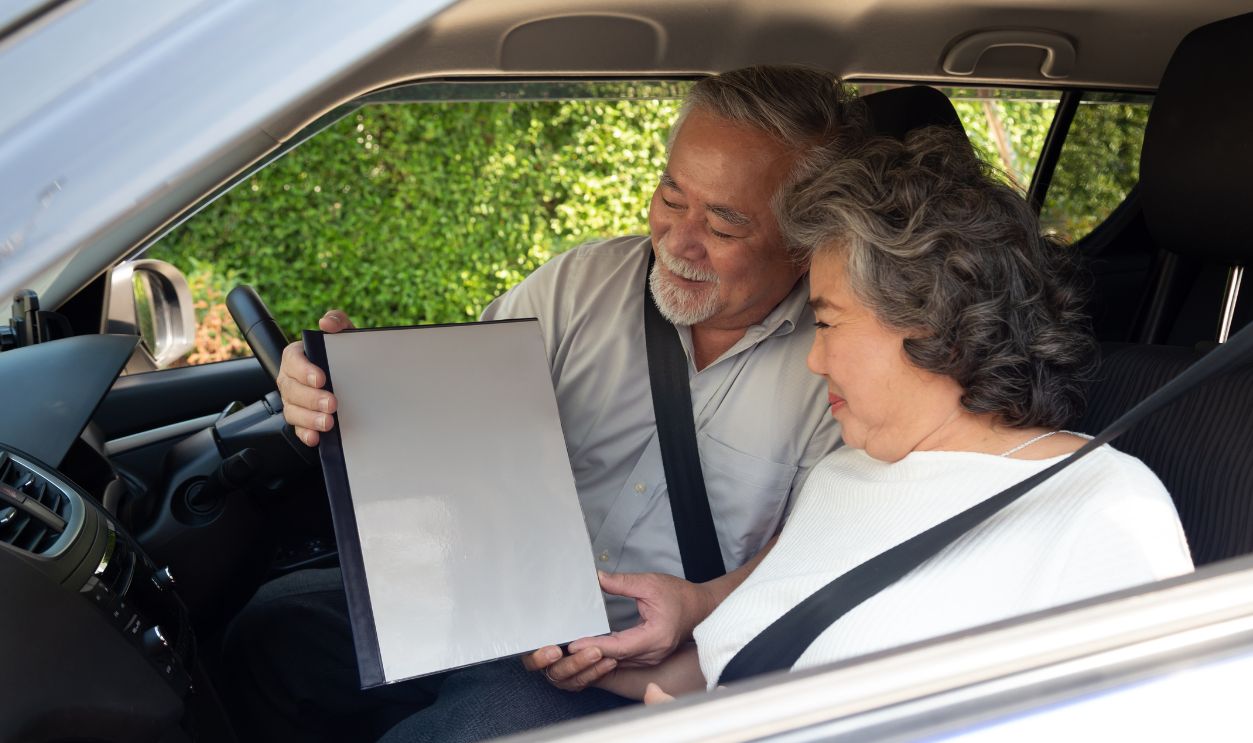 Happy Asian senior couple sitting in car and holding insurance document file