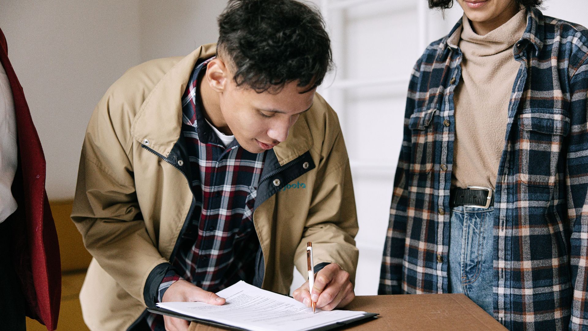 Young adults signing documents on moving day, finalizing new home purchase.