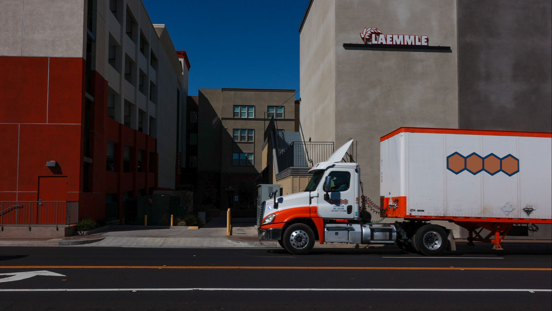 A delivery truck parked on a city street under bright sunlight in front of modern buildings.