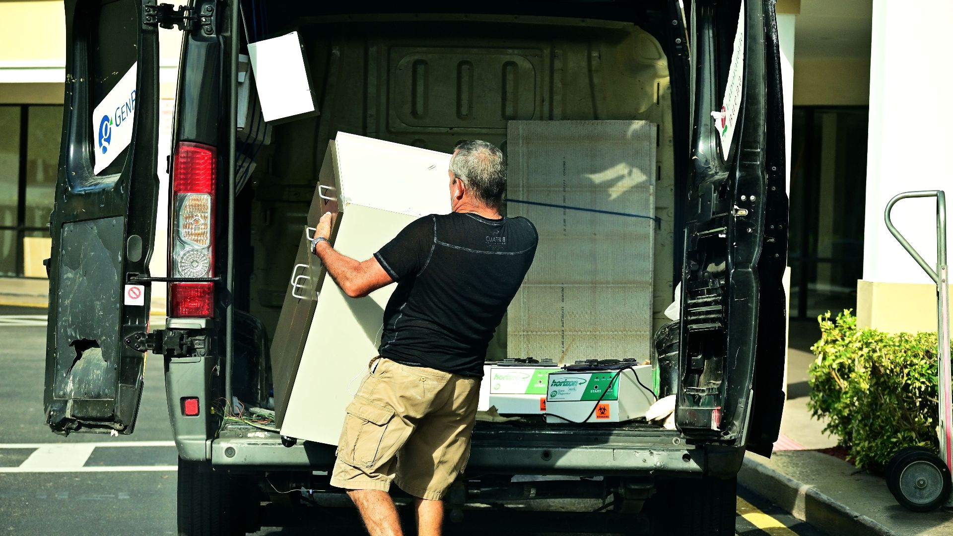 Adult man loading furniture into an open van in a parking lot, daytime setting.