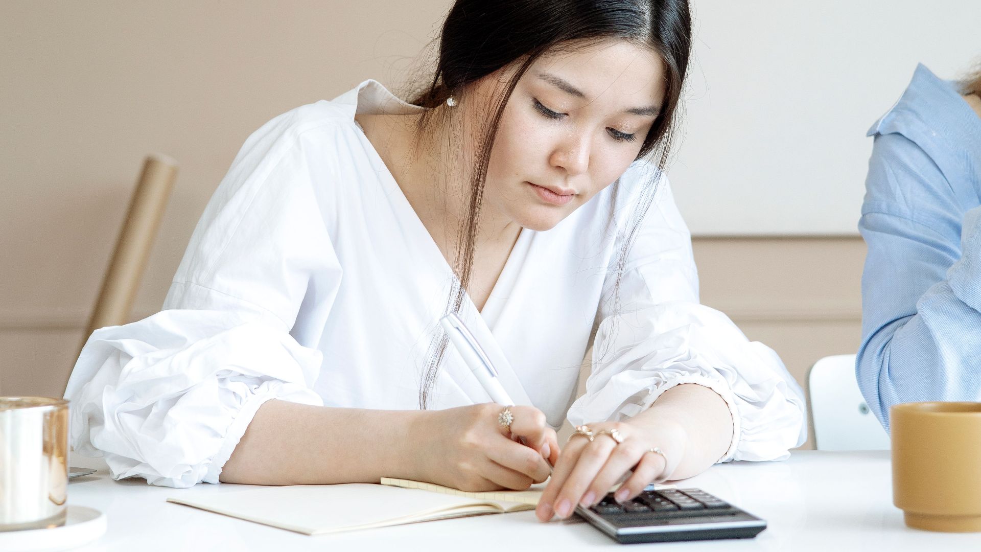 An adult woman attentively doing calculations on a calculator at a desk in a modern office setting.