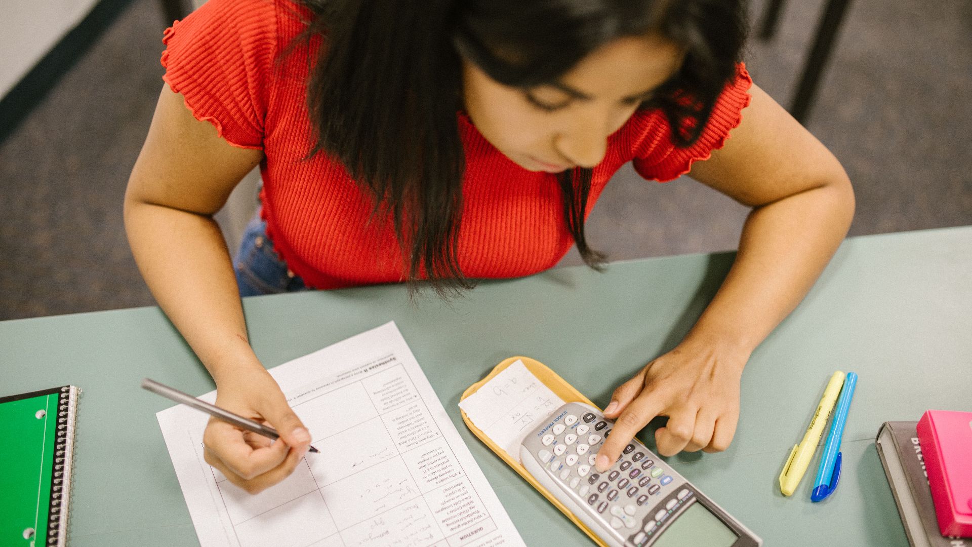 College student focusing on math test, using a calculator at a desk.