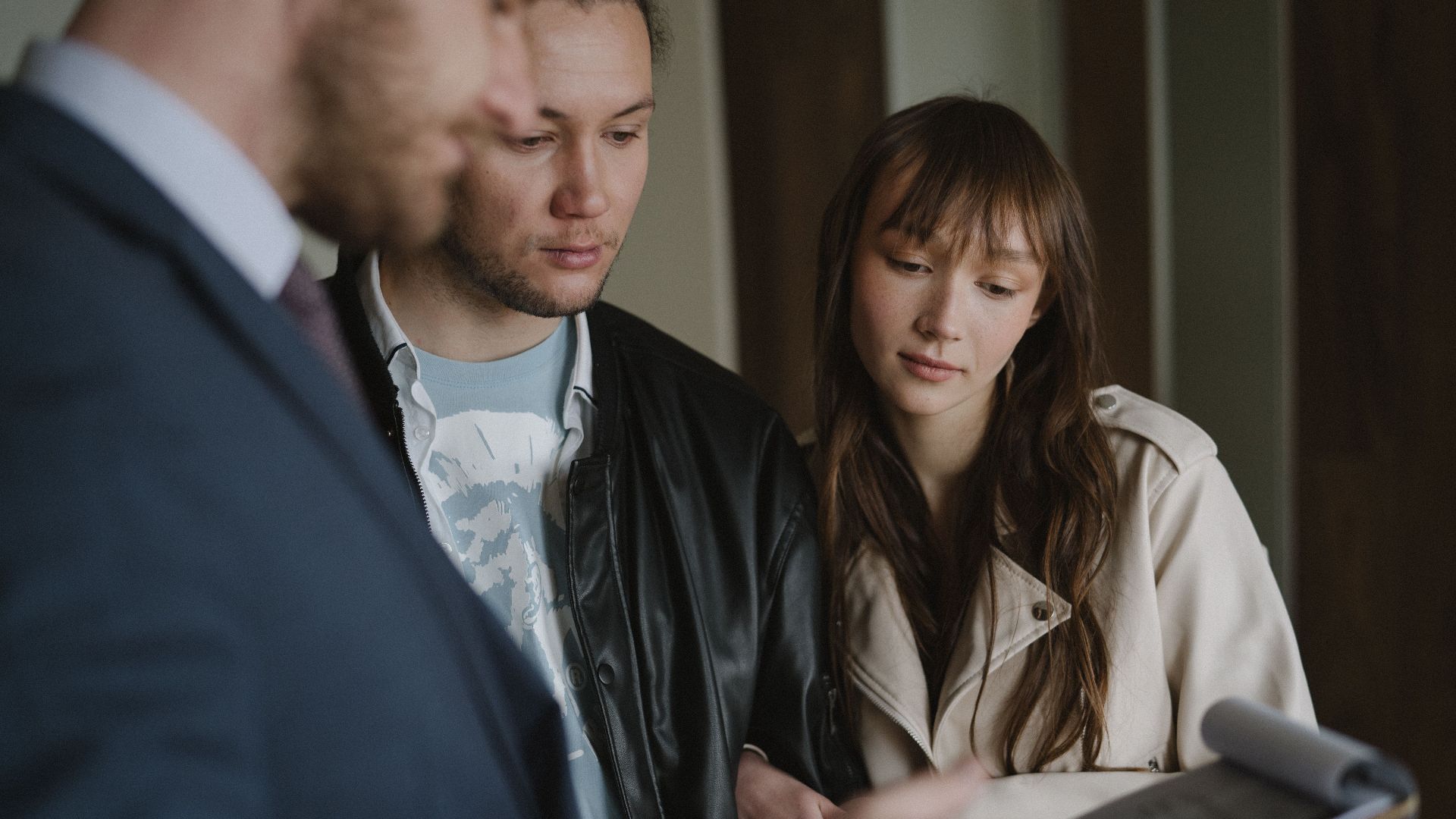 A couple discusses home buying details with a realtor inside a modern apartment.