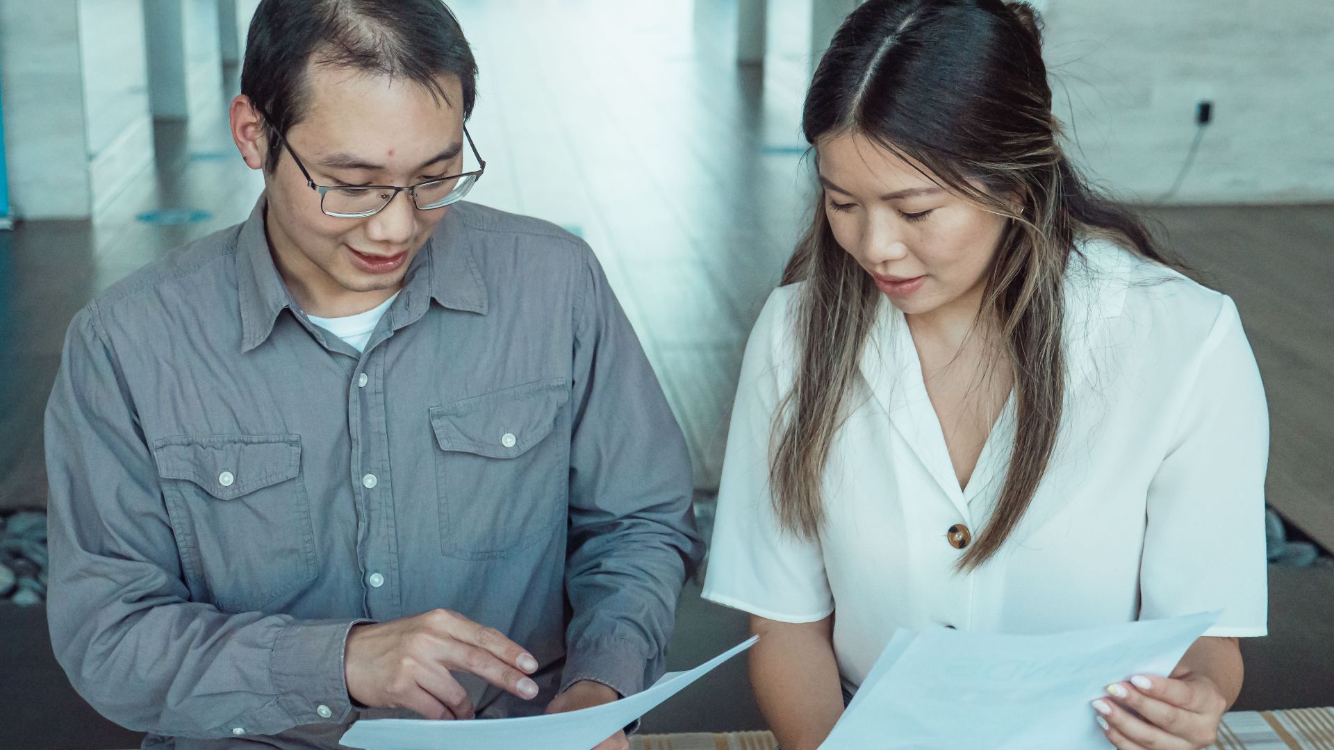 Two coworkers reviewing documents in a modern office, focused on teamwork and planning.