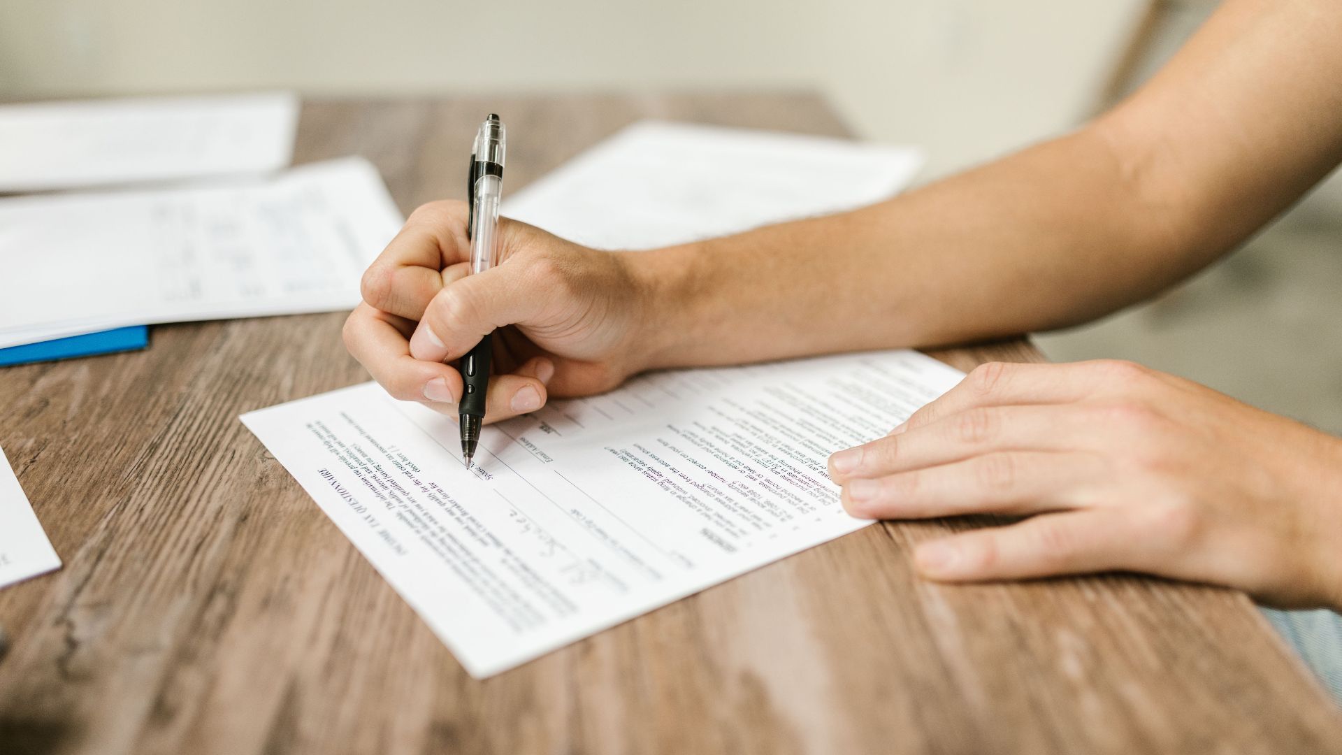 Hand filling out paperwork with a pen, showcasing focus on document completion.