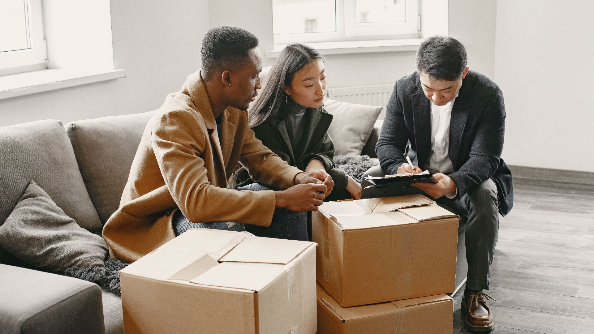 Multiracial couple signing real estate papers at home with a realtor. Cardboard boxes suggest moving in.
