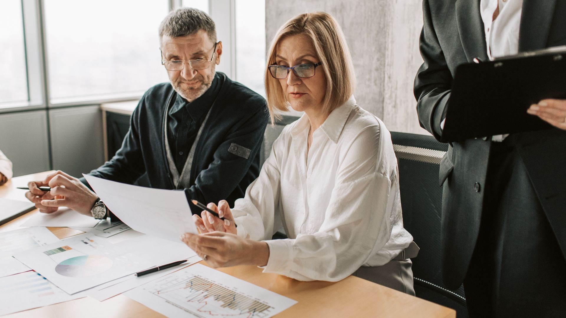 Business professionals engaged in a meeting, analyzing documents and charts in a modern office.