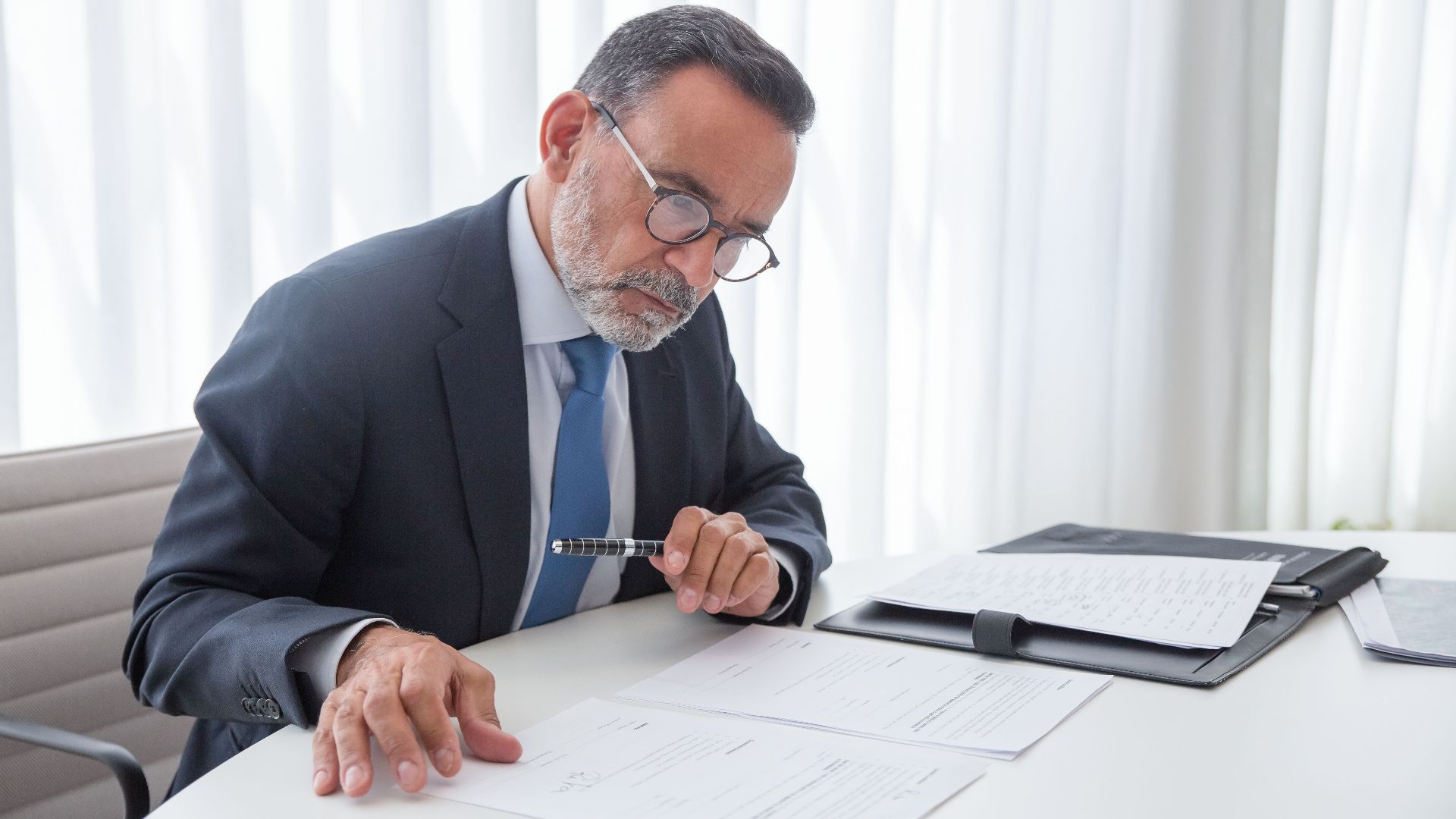 Elderly businessman focused on reviewing documents at his office desk.